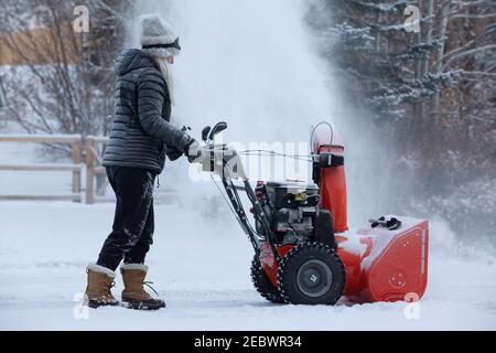 Donna anziana che sgombrava la neve con un soffiatore di neve Foto Stock