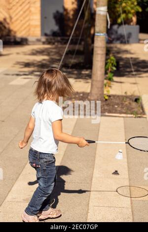 un bambino giocoso in una t-shirt bianca gioca il bambinton in parcheggia in una giornata estiva di sole Foto Stock