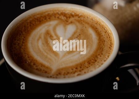 Piatto bianco su una tazza di caffè con un fiore a forma di cuore disegnato con schiuma di latte. Da utilizzare come sfondo, messa a fuoco selettiva Foto Stock