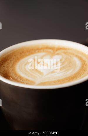 Piatto bianco su una tazza di caffè con un fiore a forma di cuore disegnato con schiuma di latte. Da utilizzare come sfondo, messa a fuoco selettiva Foto Stock