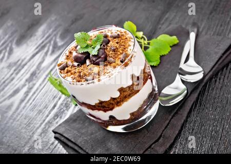 Dessert Foresta Nera di ciliegie, biscotto al cioccolato e formaggio casolare morbido con panna in un bicchiere su tovagliolo, menta, bacche in una ciotola e un cucchiaio su da Foto Stock
