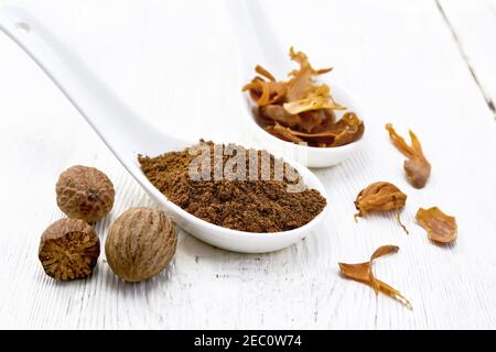 Noce moscata macinata e arillus di noce moscata secca in due cucchiai, noci intere su fondo bianco di legno Foto Stock