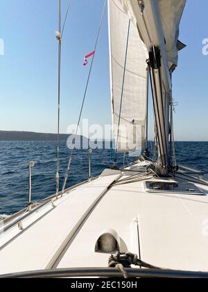 Yacht a vela lontano dalle teste del porto di Sydney, in una giornata tranquilla e soleggiata. Vista dall'abitacolo della barca all'orizzonte, con North Head Foto Stock