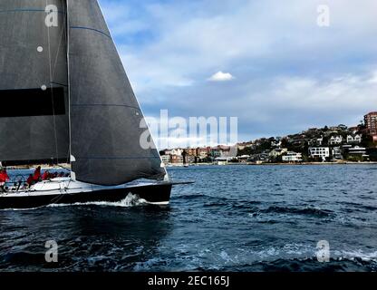 Calmo condimento di uno yacht che corre nel porto di Sydney con il suo spinnaker rosso schierato. Vista a scatto media con cielo nuvoloso Foto Stock