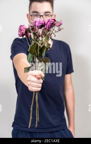 Giovane ragazzo in bicchieri con un bouquet di rose appassite e mostra fig. Infelice concetto di amore Foto Stock