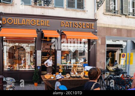 Strasburgo, Francia - 29 luglio 2017: Donna sorridente felice di fronte al suo stand vendita di prodotti da forno multipli e dolci tradizionali alsaziani di fronte a Boulangerie Patisserie grande vetrina Foto Stock