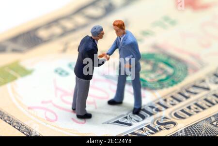 Uomini d'affari che scuotono le mani sul dollaro americano. Piccoli uomini d'affari figurine su sfondo di denaro. Concetto di finanza o di crescita economica. Rendere redditizio de Foto Stock