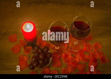Due bicchieri da vino rosso, uva, candela bruciante e foglie di rosa sul tavolo. Concetto di San Valentino. Foto Stock