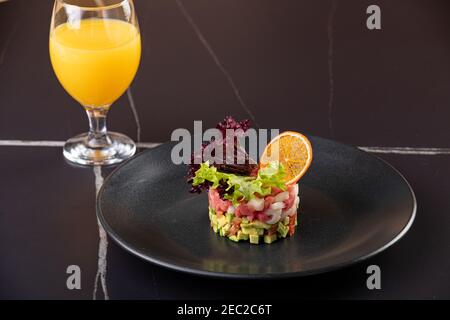 Tartaro di tonno fresco crudo con spezie da primo piano su un piatto e bicchiere con succo. Orizzontale su fondo nero Foto Stock