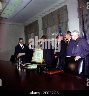 Firma della proclamazione - Voluntary Overseas Aid Week, 11:30. Il rabbino Herbert A. Friedman, Vice Presidente Esecutivo dell'appello ebraico Unito (a sinistra), legge da un articolo in occasione della presentazione del presidente John F. Kennedy (al centro, torna alla telecamera) Con un scroll incorniciato citando il suo u0022vigoroso campionato di assistenza costruttiva al bisognoso abroadu0022 durante la firma della proclamazione che designa la settimana del 9 aprile 1962, come Volontario Overseas Aid Week. Altri leader delle organizzazioni umanitarie e religiose americane guardano avanti. (L-R) non identificato (nella parte posteriore, per lo più nascosto); Rabbi Friedman; Richar Foto Stock