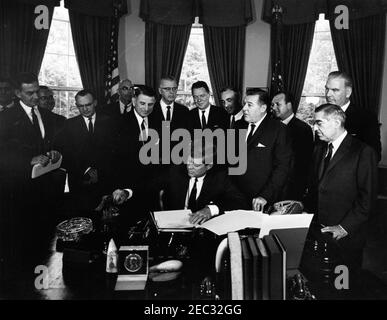 205 Legge pubblica 87-447, Legge sulla Televisione educativa, 12:00 PM. Il presidente John F. Kennedy (seduto) firma la legge sulla televisione educativa. Stand (L-R): Unidentified (in ombra); Senator Clifford P. Case (New Jersey); Presidente della Federal Communications Commission (FCC), Newton Minow; Congressman John E. Moss (California); Unidentified; Congressman Oren Harris (Arkansas); Senator Norris Cotton (New Hampshire); Congressman Hale Boggs (Louisiana); Secretary of Abraham, Health, e Health, Abraham Reducation, Harris Welfare; Abraham, Harris Health, e Welfare; Senator Warren G. Magnuson (Washington); avvocato, Leonard H. Marks (i Foto Stock