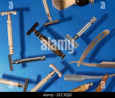Diversi tipi di rasoi, inclusi quelli di sicurezza e diritti, lama, spazzola e profumo su sfondo blu. Vista dall'alto. Foto Stock