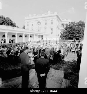 Visita del 1 ° corpo di Pace Volontarii per andare all'estero, 16:10. Il presidente John F. Kennedy guarda come il direttore del corpo della Pace R. Sargent Shriver parla durante una cerimonia per il primo gruppo di volontari del corpo della Pace in partenza, in partenza per Tanganyika e Ghana, nel Rose Garden, Casa Bianca, Washington, D.C. notano giornalisti e fotografi, Compreso Washington corrispondente per la Guy Gannet Publishing Company del Maine, May Craig. [Per un elenco completo dei partecipanti, vedere White House Central Subject Files, Box 670, Folder 1: U0022PC 5 Peace Corps Program (Executive, 1-20-61 - 4-10-62) Foto Stock