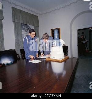 Il presidente Kennedy con una capsula Gemini modello. Il presidente John F. Kennedy si trova accanto a un modello in scala di una capsula Gemini nella stanza del gabinetto della Casa Bianca, Washington, D.C.; Il modello è stato dato al presidente Kennedy come regalo di Natale dal personale della McDonnell Aircraft Corporation, dopo la visita del presidente 2019 allo stabilimento di McDonnellu2019s St. Louis il 12 settembre 1962. Air Force Aide al presidente, Brigadier General Godfrey T. McHugh, si trova a sinistra. Visibile attraverso la porta a destra: Militare Aide al presidente, generale Chester V. Clifton; John F. Kennedy, Jr. (Seduta Foto Stock