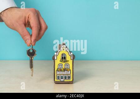 Modello di casa e chiave in mano, concetto immobiliare, spazio copia a colori turchese. Foto Stock