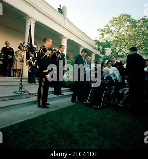 Il presidente Kennedy saluta i destinatari della Medaglia d'onore del Congresso, ricevimento militare annuale, alle 18:03. Il presidente John F. Kennedy visita con il generale maggiore dell'esercito americano in pensione, Charles E. Kilbourne (a destra, in sedia a rotelle), ad un ricevimento militare in onore dei destinatari della medaglia d'onore del Congresso. Anche nella foto: Segretario della Marina, Fred Korth (all'estrema sinistra, in piedi sul colonnato); Aide militare al Presidente, Generale Chester V. Clifton (a sinistra, in primo piano); Aide navale al Presidente, Capitano Tazewell Shepard (a destra del Generale Clifton). Rose Garden, Casa Bianca, Washington, D.C. Foto Stock