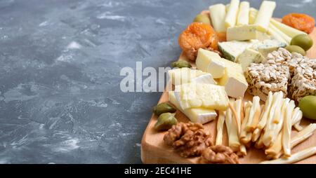 Diversi tipi di formaggi, albicocche secche, pani a grani interi, noci, olive, capperi su tavola di legno. Formaggio a tavola, spuntini. Spazio di copia Foto Stock