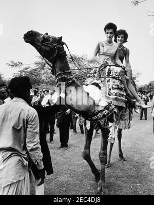 Prima Lady Jacqueline Kennedyu2019s (JBK) viaggio in India e Pakistan: Karachi, Sindh, Pakistan, giro in cammello e visita con il camel driver Bashir Ahmad e la famiglia. First Lady Jacqueline Kennedy (a destra) e sua sorella, la Principessa Lee Radziwill di Polonia (a sinistra), cavalcano un cammello attraverso i terreni della residenza del presidente Mohammad Ayub Khanu0027s a Karachi, Sindh, Pakistan. Foto Stock