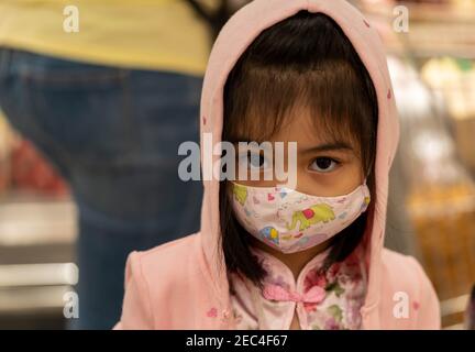 Bambina con maschera in tessuto proteggersi da Coronavirus quando il bambino va al supermercato. Ragazza asiatica piccola che indossa la maschera in un mercato Foto Stock