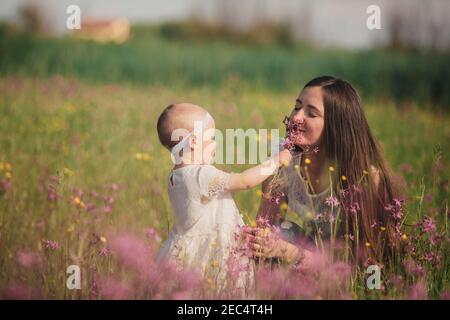 la mamma giovane e la bambina carina camminano e giocano sul campo con fiori selvatici. la famiglia si diverte in estate, giorno di sole. infanzia e parentismo Foto Stock