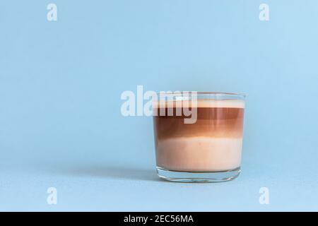 Mini tazza di caffè multistrato in una tazza di vetro su sfondo blu Foto Stock