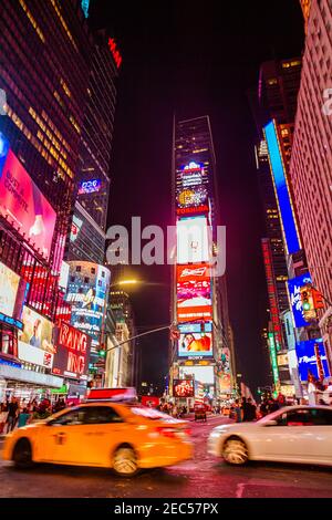 Una vista notturna di Times Square, la più famosa attrazione turistica del mondo, guardando a nord con un taxi sfocato e un'auto che passa Foto Stock