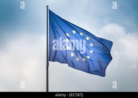 Bandiera dell'Unione europea che oscilla nel vento sul flagpole contro il cielo con le nuvole nel giorno di sole, primo piano Foto Stock