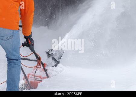 un uomo adulto ha sparato dalla schiena rimuovendo la neve con un dispositivo speciale di soffiaggio. Attrezzatura per la rimozione della neve con un cavo. Spingere uno strumento per pulire un marciapiede. Un processo di soffiatura della neve. Foto di alta qualità Foto Stock