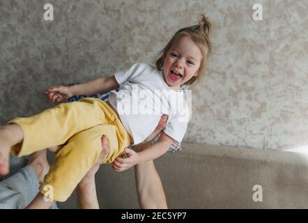 il padre gioca con la figlia sul divano, la alza in alto tra le braccia, la gioia e la felicità dei bambini. Foto Stock