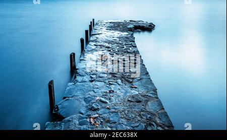 Molo costruito in pietra che si estende nelle acque ferme di Coniston Water, Lake District National Park, Cumbria, Regno Unito Foto Stock