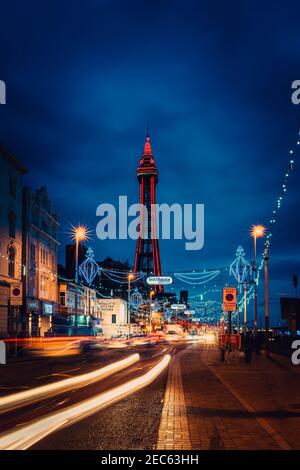La famosissima Blackpool Tower e le illuminazioni fotografate di notte con i sentieri per auto in primo piano Foto Stock