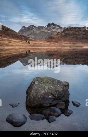 Bella alba invernale su Blea Tarn nel Lake District con Pikes Langdale innevate in lontananza Foto Stock