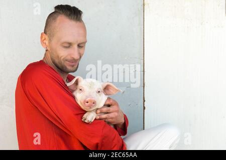 Carino ritratto di porcini sulle mani del proprietario dell'azienda. Coltivatore che tiene il maiale giovane grazioso. Focus sul piggy. Foto Stock