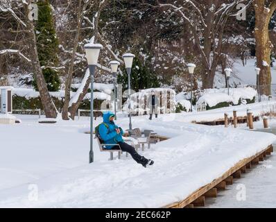 Maribo Danimarca - Marte 3. 2018: Giorno d'inverno vicino al lago, un uomo seduto su una panchina e una donna che cammina sul sentiero Foto Stock
