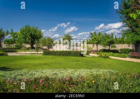 Piccolo parco cittadino con panchine, fiori, siepi verdi, alberi e erba. Nin città cimitero e catena montuosa delle Alpi Dinariche in background, Croazia Foto Stock