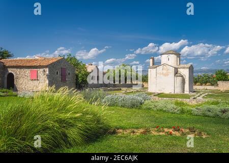 Antica, datata il 9 ° secolo, Chiesa della Santa Croce a Nin con erba e fiori di fronte e la catena montuosa delle Alpi Dinariche in background, Croazia Foto Stock