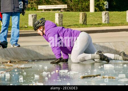 Un giovane uomo strisciato sul ghiaccio dopo aver scivolato mentre cammina su un laghetto ghiacciato. Whitestone Pond, su Hampstead Heath, è il punto più alto di Londra a 135 metri sopra il bacino londinese. Regno Unito Meteo. Hampstead, Londra, Regno Unito 13 febbraio 2021. Foto Stock
