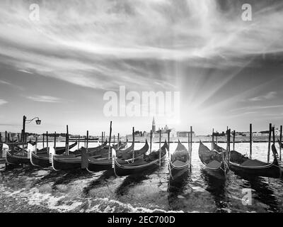 Scala di grigi. Gondole parcheggiate su Piazza San Marco e l'argine del Palazzo Ducale e il sole del tramonto (Venezia, Italia). Foto Stock