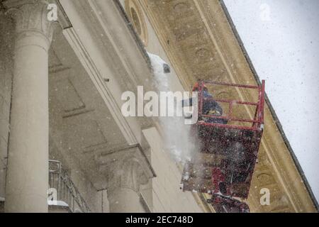 Mosca, Russia, 13 febbraio 2021: Una squadra di lavoratori pulisce il tetto di un edificio dalla neve con pale dopo una pesante nevicata Foto Stock