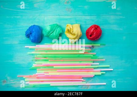 Sacchetti di plastica colorati e cannucce su sfondo turchese di legno. Disposizione piatta. Divieto di concetto di plastica Foto Stock