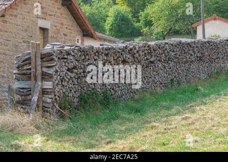 Legna da ardere per il riscaldamento si trova lungo il muro di mattoni casa. Riscaldamento a legna e case in pietra sono tradizionali nel villaggio di Bourgogne, Francia. Foto Stock