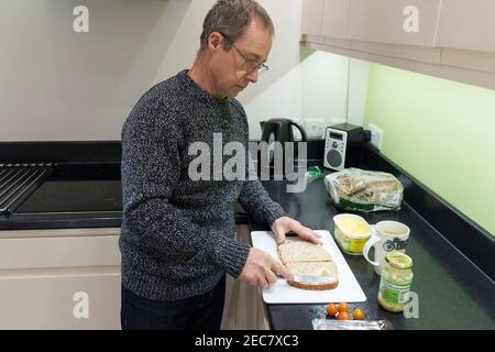 Panino rendendo pensionato maschio facendo un panino di manzo e pomodoro in casa in cucina durante il blocco 2020. Un'immagine di sé di sette presi. Foto Stock