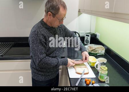 Panino rendendo pensionato maschio facendo un panino di manzo e pomodoro in casa in cucina durante il blocco 2020. Un'immagine di sé di sette presi. Foto Stock