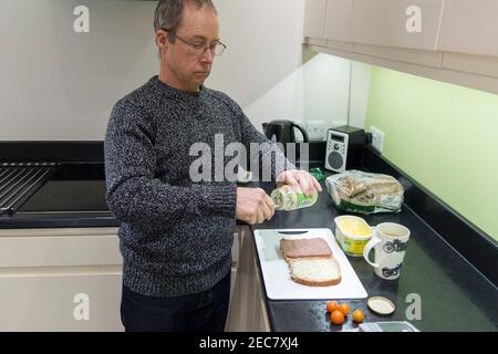 Panino rendendo pensionato maschio facendo un panino di manzo e pomodoro in casa in cucina durante il blocco 2020. Un'immagine di sé di sette presi. Foto Stock