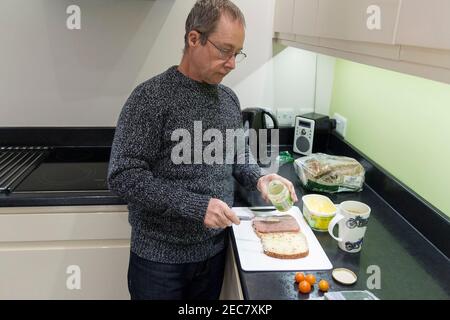 Panino rendendo pensionato maschio facendo un panino di manzo e pomodoro in casa in cucina durante il blocco 2020. Un'immagine di sé di sette presi. Foto Stock