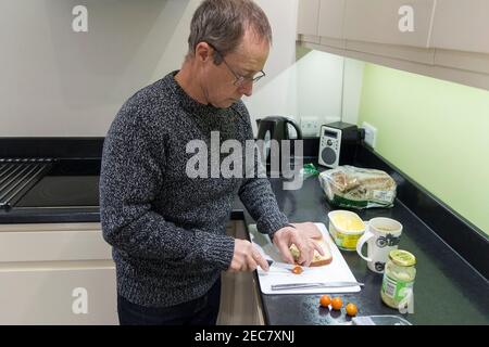 Panino rendendo pensionato maschio facendo un panino di manzo e pomodoro in casa in cucina durante il blocco 2020. Un'immagine di sé di sette presi. Foto Stock