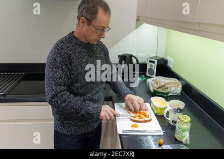 Panino rendendo pensionato maschio facendo un panino di manzo e pomodoro in casa in cucina durante il blocco 2020. Un'immagine di sé di sette presi. Foto Stock