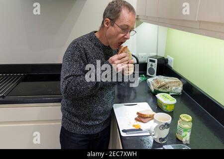 Panino rendendo pensionato maschio facendo un panino di manzo e pomodoro in casa in cucina durante il blocco 2020. Un'immagine di sé di sette presi. Foto Stock