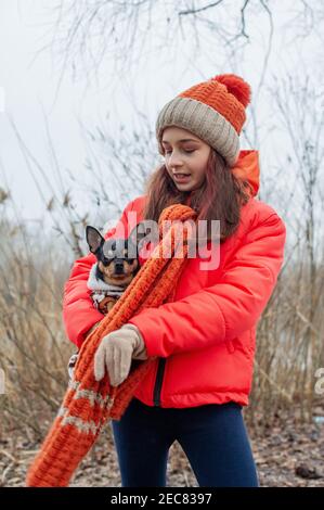 Ragazza e cane in abiti invernali. Ragazza adolescente in giacca arancione, cappello e sciarpa. Ragazza e chihuahua Foto Stock