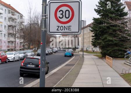 30 km all'ora segnale limite di velocità accanto a una strada in un'area residenziale con parcheggio auto sulla strada. Foto Stock